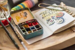 watercolor paint and art supplies and sketchbook on a wooden table